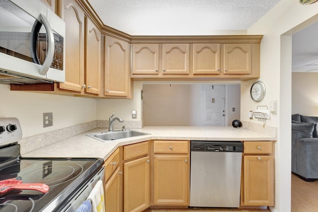 kitchen with stainless steel appliances, a sink, light countertops, light brown cabinets, and a textured ceiling