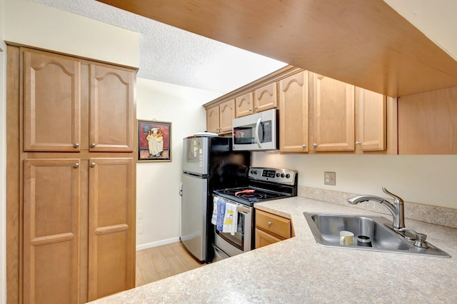 kitchen featuring appliances with stainless steel finishes, a sink, light countertops, light brown cabinets, and light wood-style floors