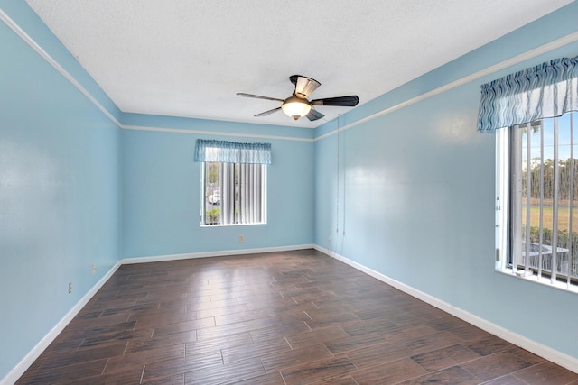 unfurnished room with plenty of natural light, ceiling fan, dark wood finished floors, baseboards, and a textured ceiling