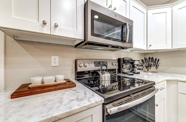 kitchen with appliances with stainless steel finishes, white cabinetry, and light stone counters