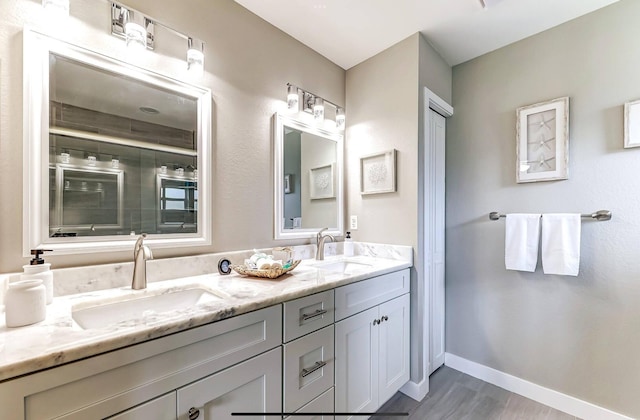 full bath featuring wood finished floors, double vanity, and baseboards