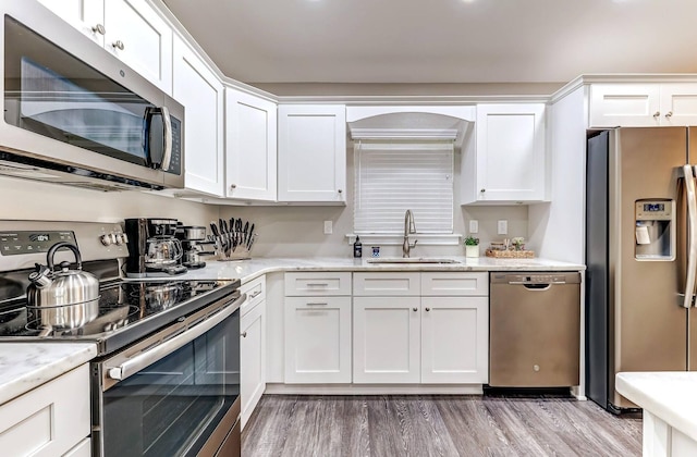 kitchen with stainless steel appliances, a sink, white cabinets, and light wood-style flooring