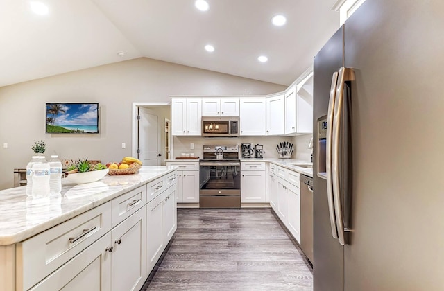 kitchen featuring stainless steel appliances, vaulted ceiling, white cabinets, dark wood finished floors, and light stone counters