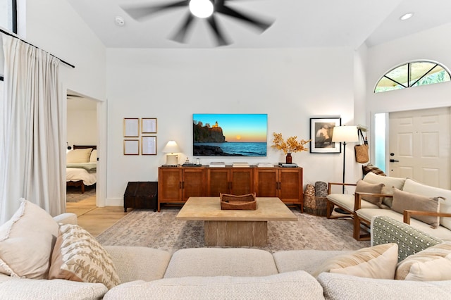 living room featuring ceiling fan, light wood-type flooring, and a towering ceiling