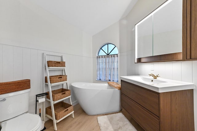 bathroom with wood finished floors, toilet, a soaking tub, vanity, and a wainscoted wall