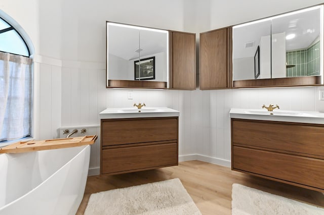 bathroom with wood finished floors, two vanities, a soaking tub, and a decorative wall