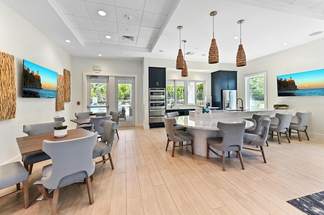 dining area with light wood-style floors, a raised ceiling, recessed lighting, and baseboards