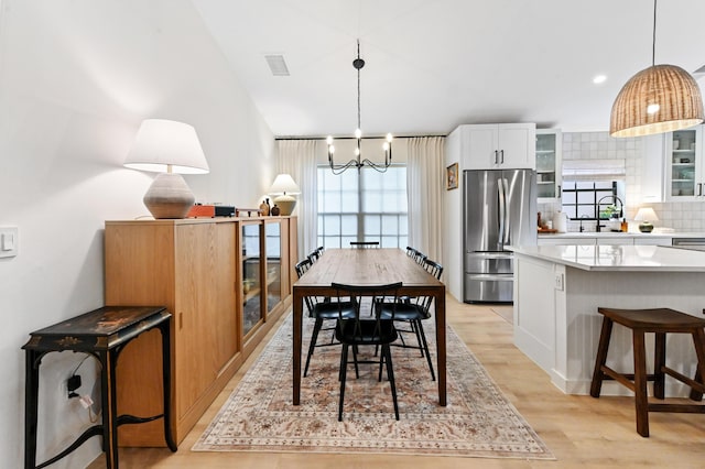 dining area with light wood finished floors, a chandelier, and lofted ceiling