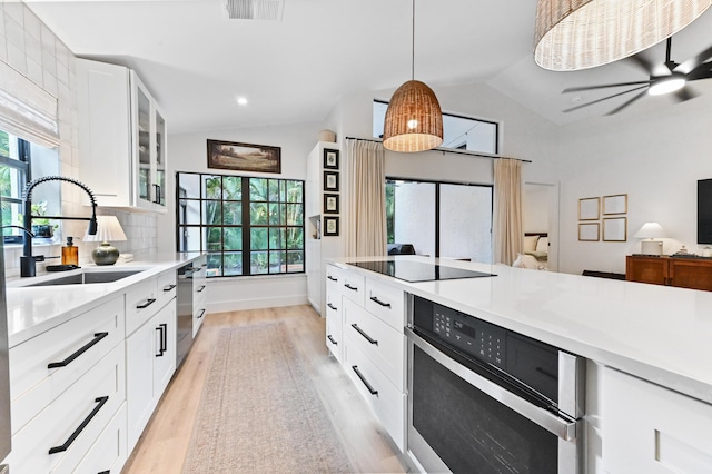 kitchen featuring a sink, stainless steel appliances, vaulted ceiling, light wood finished floors, and glass insert cabinets