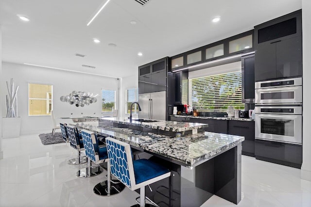 682 Cresta Cir, West Palm Beach, FL 33413 - kitchen with dark cabinetry, a sink, a kitchen breakfast bar, a large island, and light stone countertops