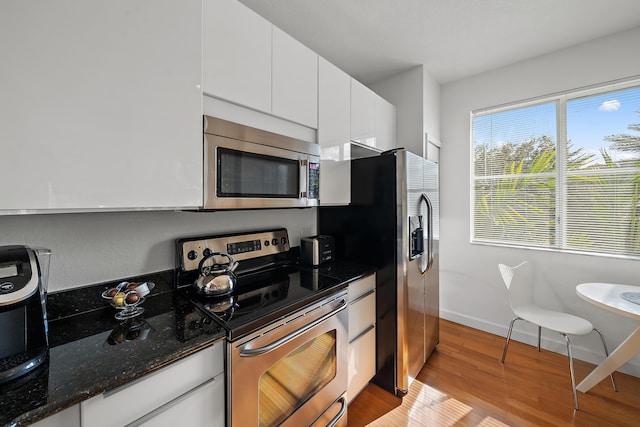 11011 Legacy Ln Unit 306, Palm Beach Gardens, FL 33410 - kitchen with appliances with stainless steel finishes, white cabinets, light wood finished floors, dark stone countertops, and baseboards