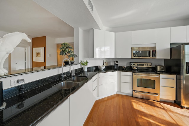 11011 Legacy Ln Unit 306, Palm Beach Gardens, FL 33410 - kitchen featuring appliances with stainless steel finishes, a sink, light wood-style flooring, white cabinetry, and dark stone countertops