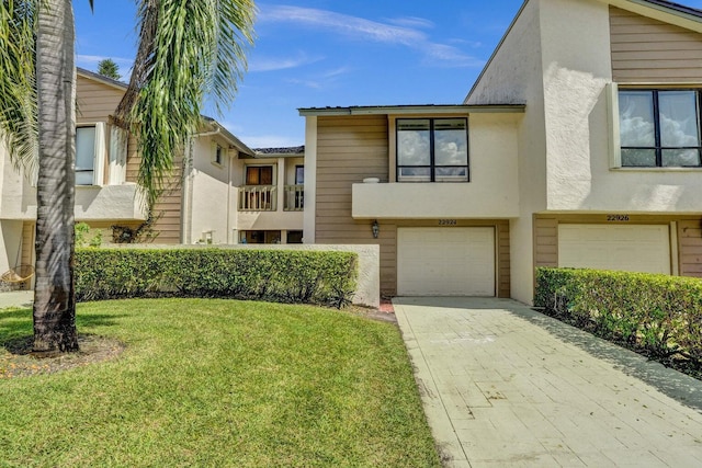 townhome / multi-family property featuring a garage, stucco siding, a front lawn, and driveway