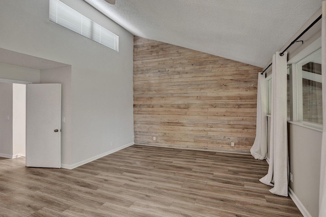 unfurnished room with wooden walls, a textured ceiling, wood finished floors, and high vaulted ceiling