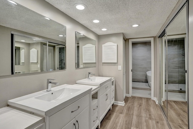 full bathroom with a textured ceiling, wood finished floors, recessed lighting, two vanities, and a stall shower