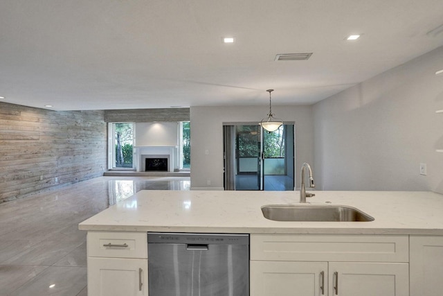 kitchen featuring dishwasher, a sink, light stone countertops, white cabinets, and wooden walls