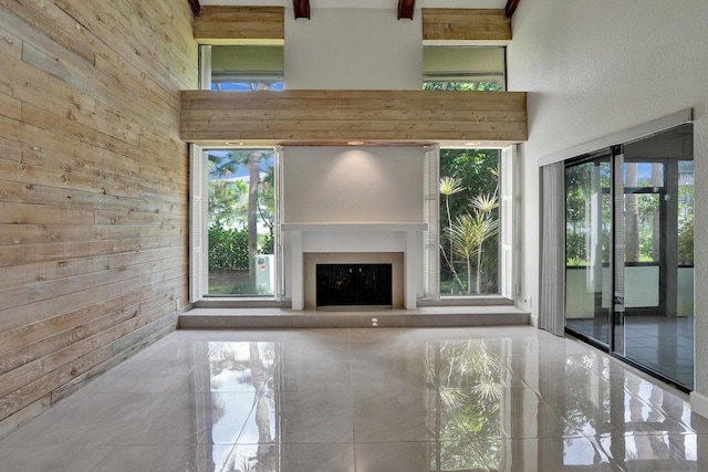 unfurnished living room featuring wooden walls, a towering ceiling, and exterior fireplace