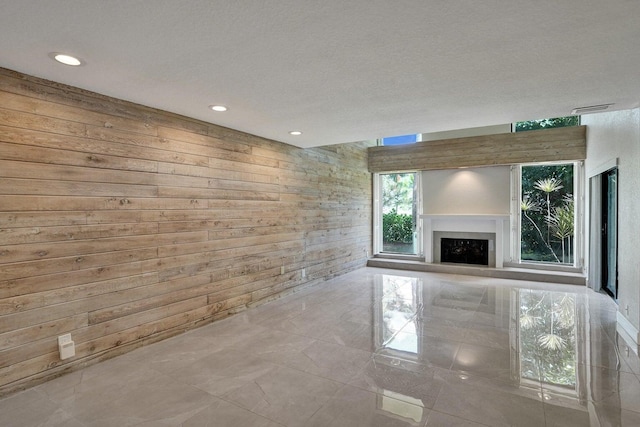 unfurnished living room with wood walls, a fireplace, recessed lighting, and a textured ceiling