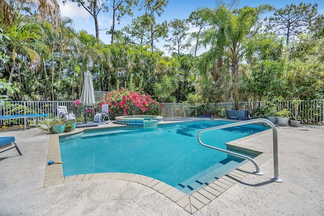 view of pool featuring fence, a patio, a pool with connected hot tub, and view of scattered trees