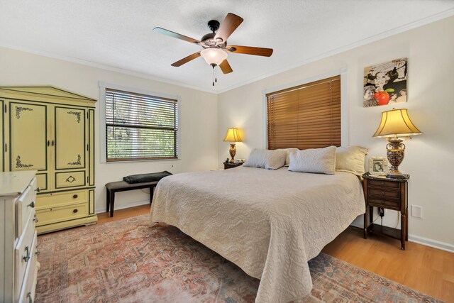 bedroom featuring light wood-type flooring, crown molding, baseboards, and ceiling fan