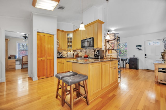 kitchen with black microwave, a breakfast bar area, light wood-type flooring, and plenty of natural light
