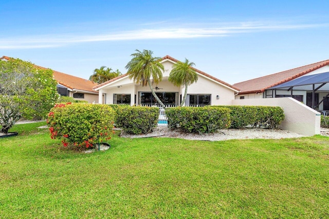 back of house featuring a lawn, stucco siding, and a tiled roof