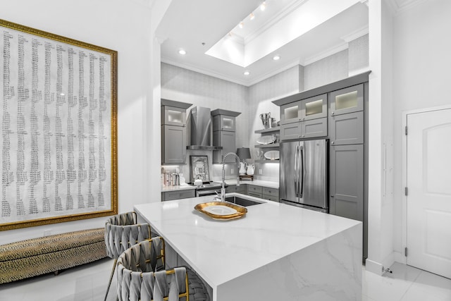 kitchen with ornamental molding, gray cabinetry, freestanding refrigerator, a sink, and an island with sink