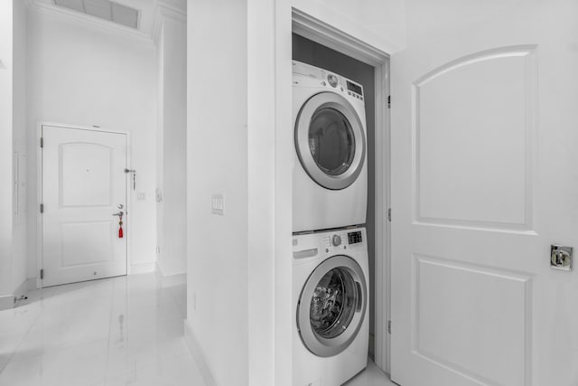 laundry area featuring stacked washer and clothes dryer, baseboards, and light marble finish flooring