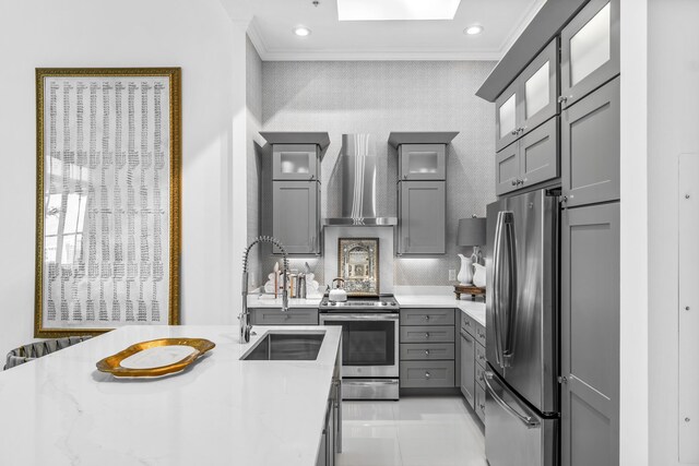 kitchen featuring appliances with stainless steel finishes, wall chimney range hood, a sink, gray cabinetry, and ornamental molding