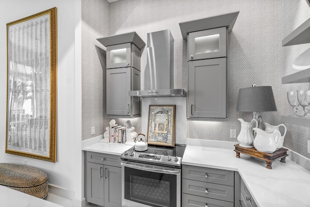 kitchen with gray cabinets, stainless steel electric stove, wall chimney exhaust hood, glass insert cabinets, and wallpapered walls