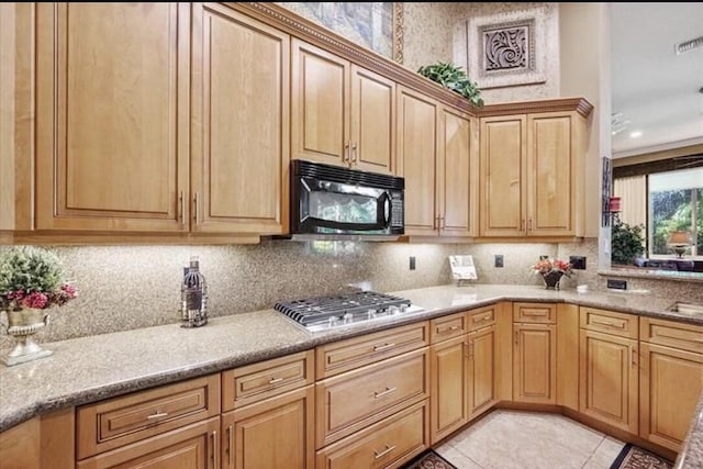 kitchen with stainless steel gas stovetop, black microwave, tasteful backsplash, light tile patterned flooring, and light stone counters