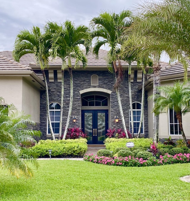 property entrance with french doors, stone siding, a lawn, stucco siding, and a tiled roof