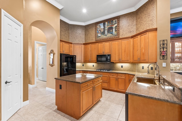 kitchen featuring black appliances, a sink, dark stone countertops, arched walkways, and crown molding