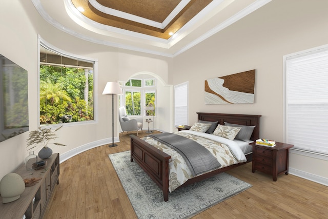 bedroom with a tray ceiling, ornamental molding, wood finished floors, baseboards, and a towering ceiling