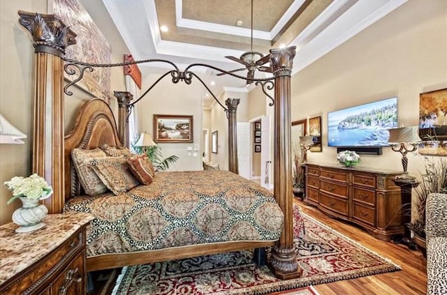 bedroom with light wood-type flooring, crown molding, a raised ceiling, and recessed lighting