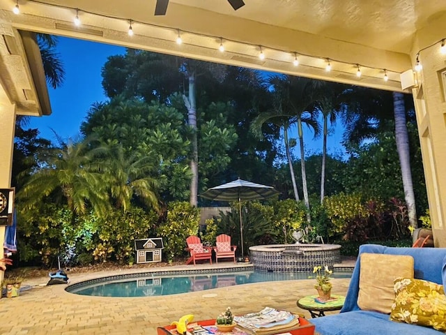 pool at night with a patio area, a pool with connected hot tub, and ceiling fan