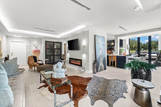 living area with light tile patterned floors, a tray ceiling, and a glass covered fireplace