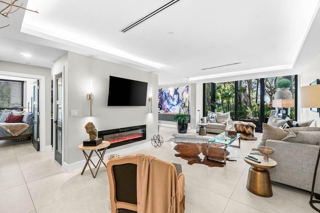 living area with light tile patterned flooring, baseboards, a glass covered fireplace, and a raised ceiling