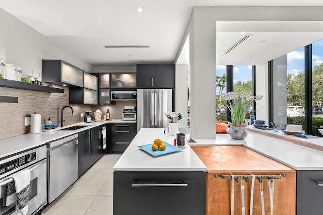 kitchen featuring a sink, stainless steel appliances, backsplash, light countertops, and light tile patterned flooring