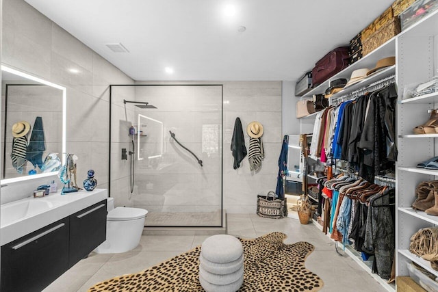 bathroom with a tile shower, toilet, tile walls, vanity, and a walk in closet