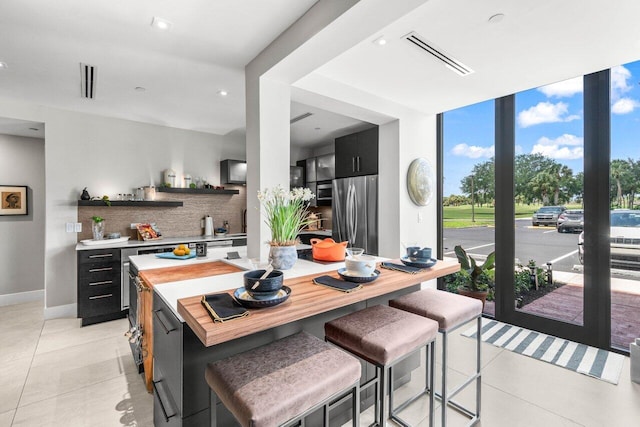 kitchen with freestanding refrigerator, backsplash, dark cabinets, light countertops, and expansive windows