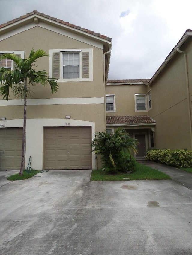 multi unit property with a tiled roof, driveway, a garage, and stucco siding
