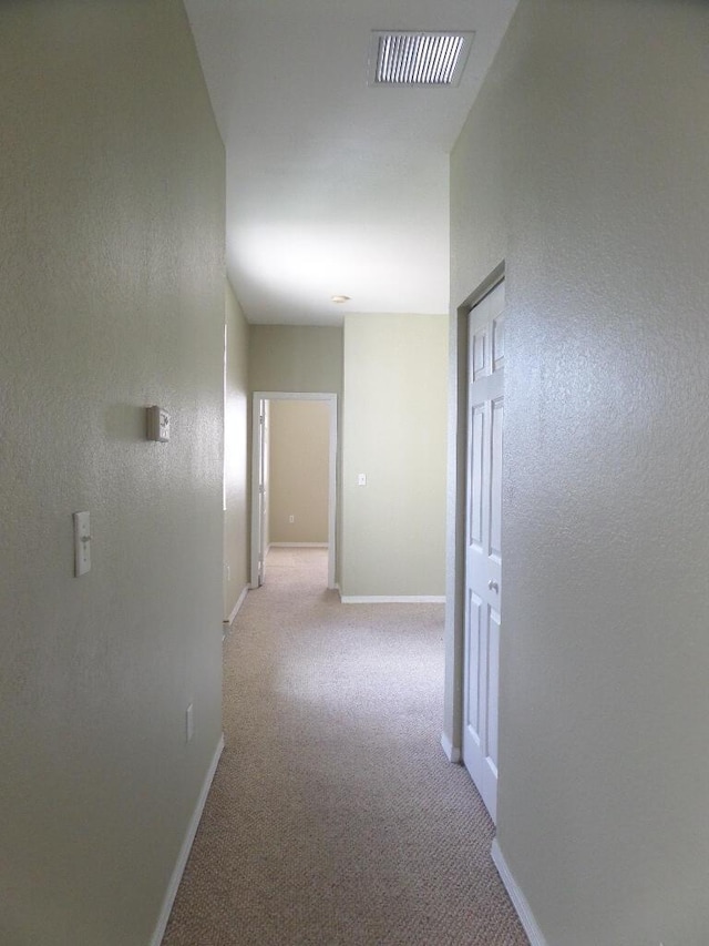 corridor featuring baseboards, light carpet, and a textured wall