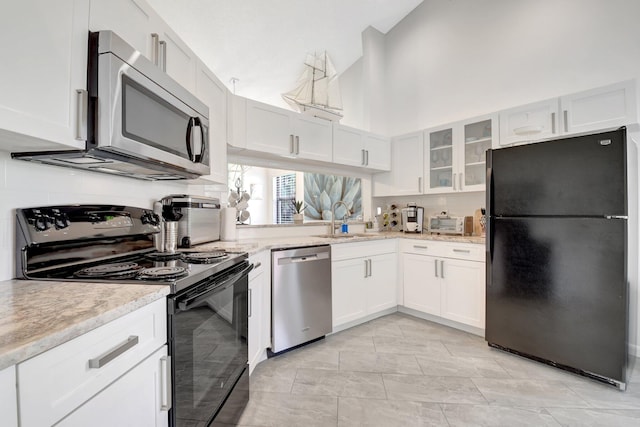 kitchen featuring black appliances, a sink, glass insert cabinets, white cabinetry, and a towering ceiling