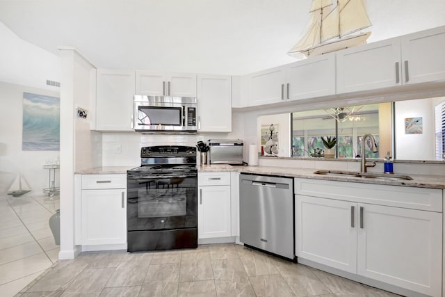 kitchen featuring appliances with stainless steel finishes, a sink, light stone counters, white cabinets, and tasteful backsplash