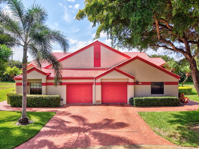 view of front of home with an attached garage, decorative driveway, a front lawn, stucco siding, and a tile roof