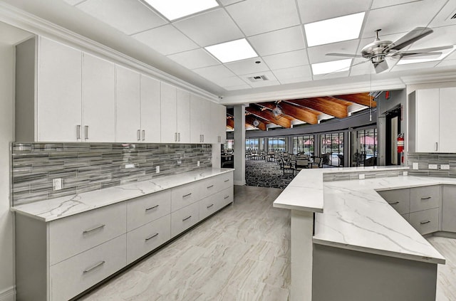 kitchen with a peninsula, ceiling fan, backsplash, gray cabinetry, and light stone countertops