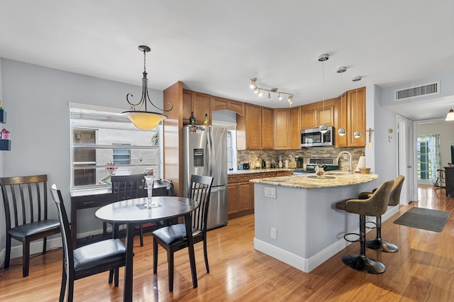 kitchen featuring appliances with stainless steel finishes, brown cabinets, light wood-type flooring, backsplash, and pendant lighting