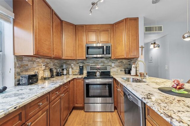 kitchen with stainless steel appliances, a sink, light wood-style flooring, and brown cabinetry