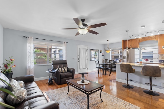 living room featuring a ceiling fan, plenty of natural light, light wood finished floors, and baseboards